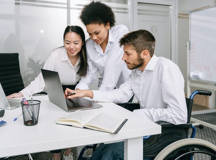Three coworkers, two women and a man in a wheelchair, work together on a laptop